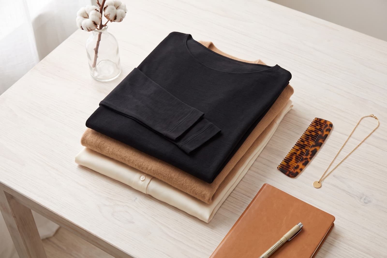 Maglia intima donna nera a manica lunga con collo a barchetta, piegata sopra un maglione cammello e una camicia color crema