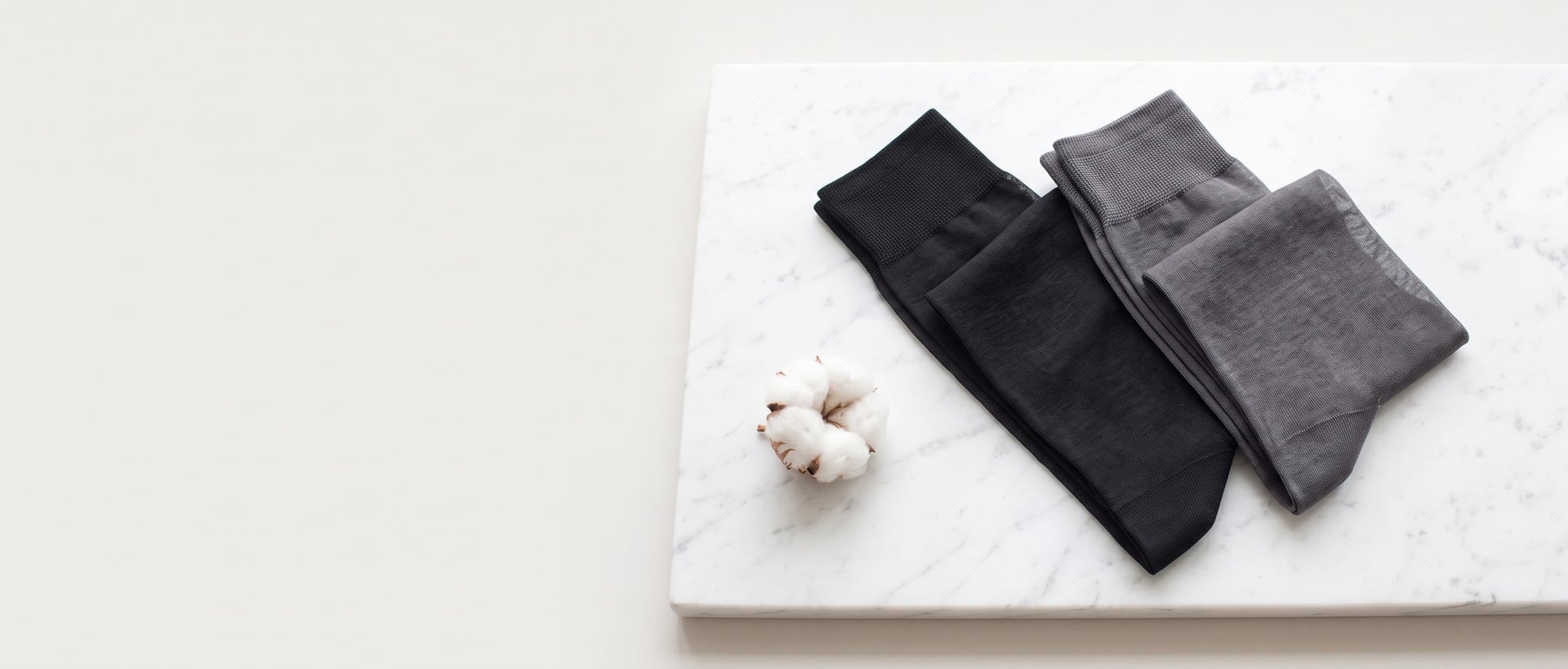 Calze sottili in cotone Filo di Scozia piegate su marmo bianco accanto a un fiore di cotone
