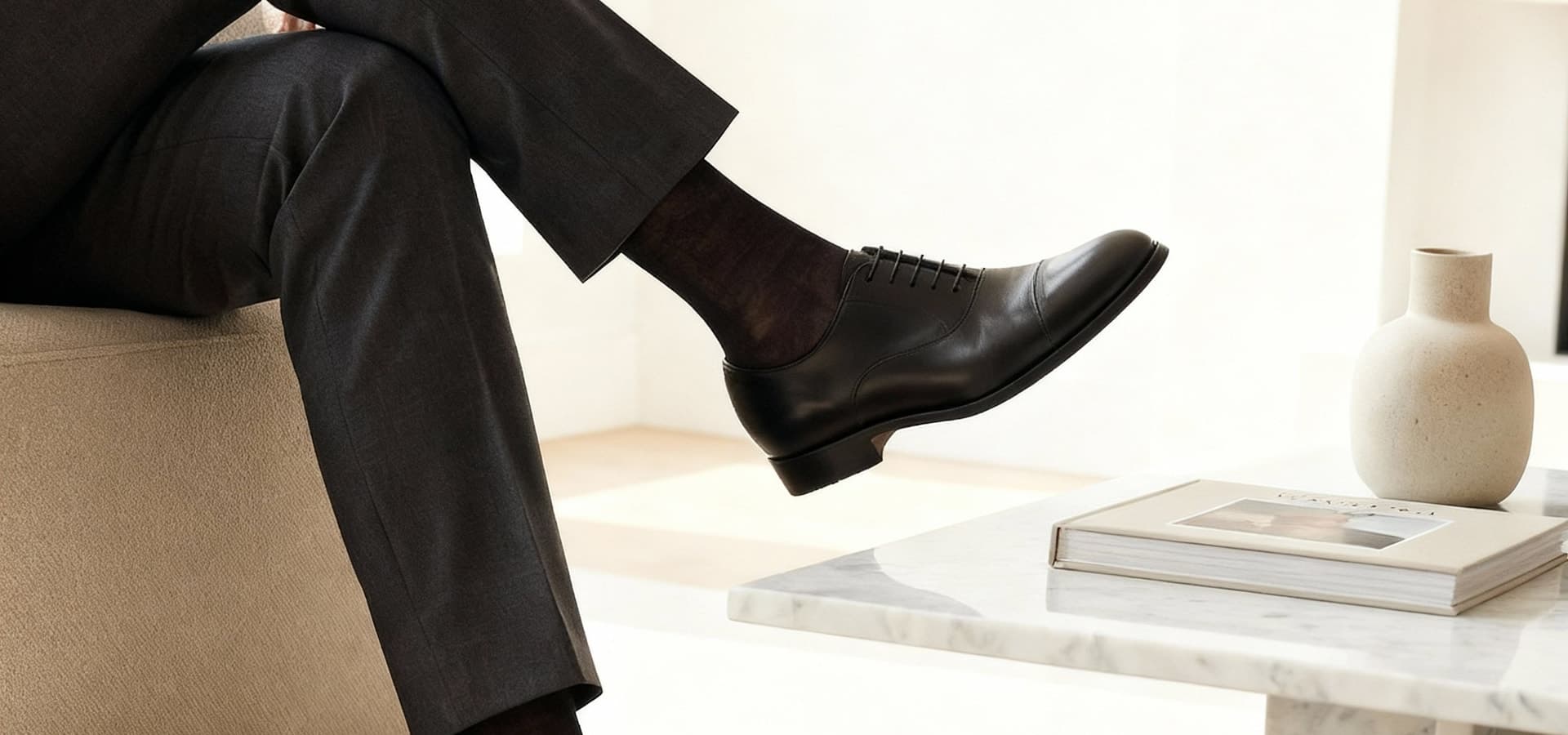 Uomo elegante seduto con calze sottili e scarpe Oxford nere su arredo minimale