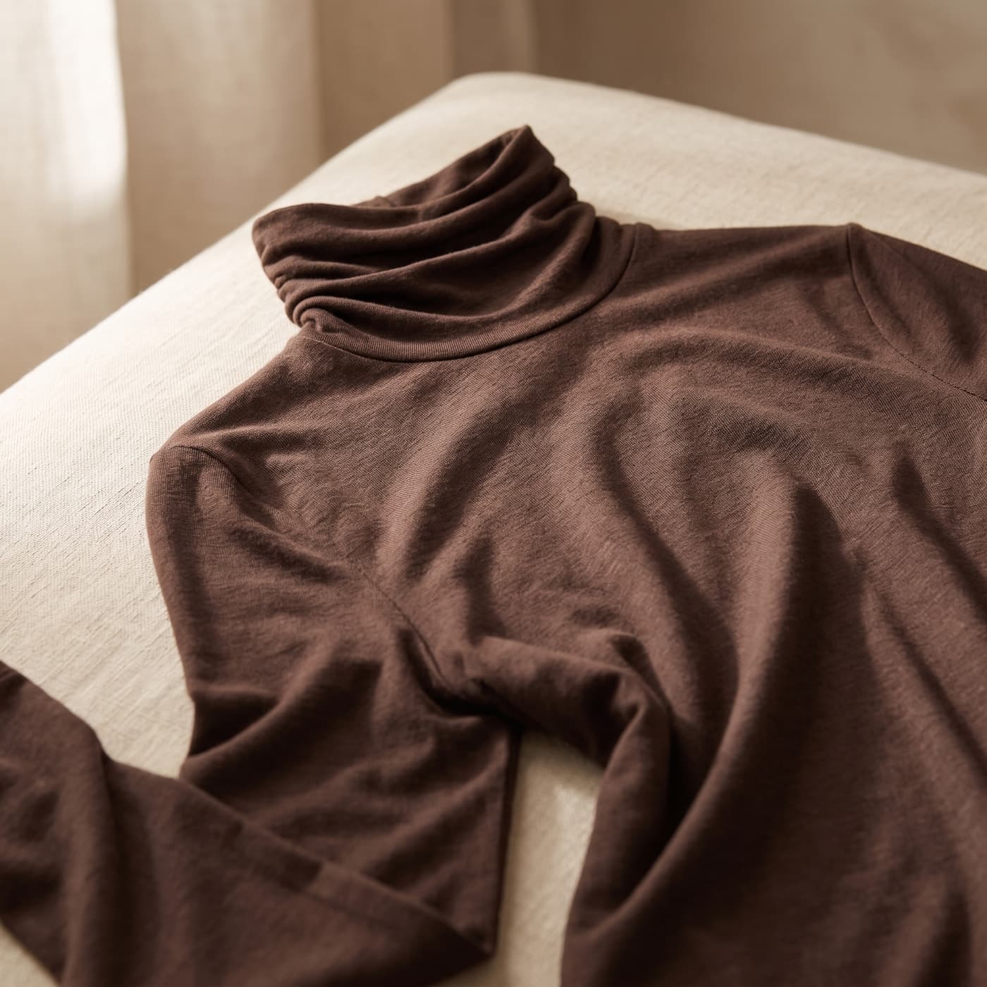 Dettaglio del tessuto in cashmere e modal della maglia dolcevita color mokka, piegata su lino