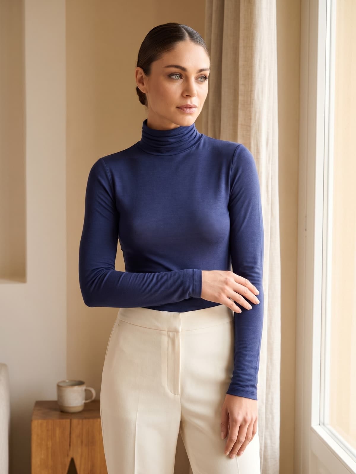 Donna con la maglia dolcevita a manica lunga in cashmere e modal blu navy, in un interno luminoso vicino alla finestra